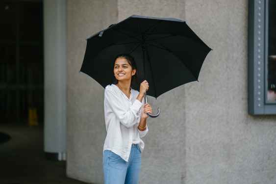 photo of woman wearing white long sleeved shirt and blue jeans holding black umbrella
